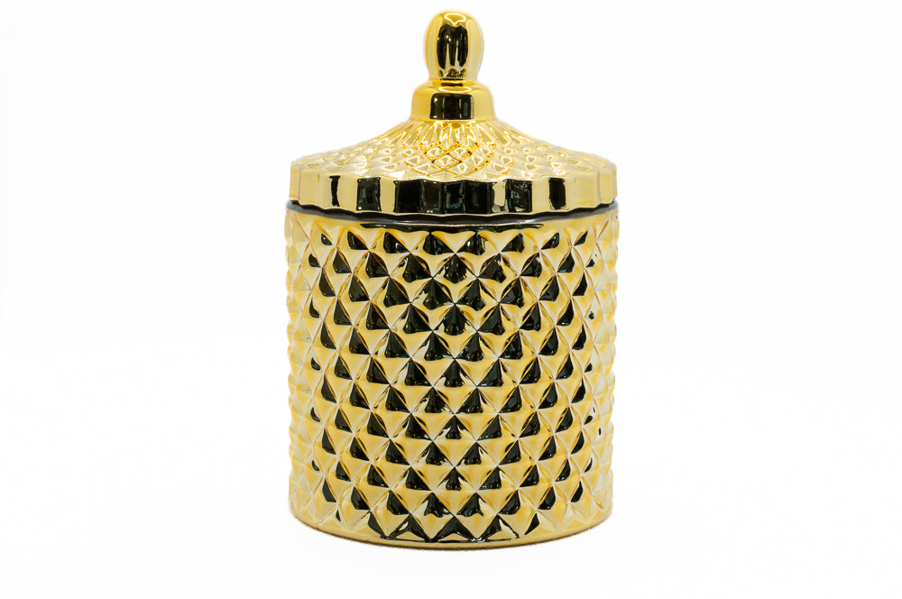 A gold coloured candle with a geometric pattern on the jar and a lid on top