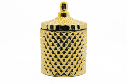 A gold coloured candle with a geometric pattern on the jar and a lid on top