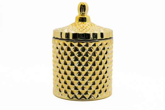 A gold coloured candle with a geometric pattern on the jar and a lid on top