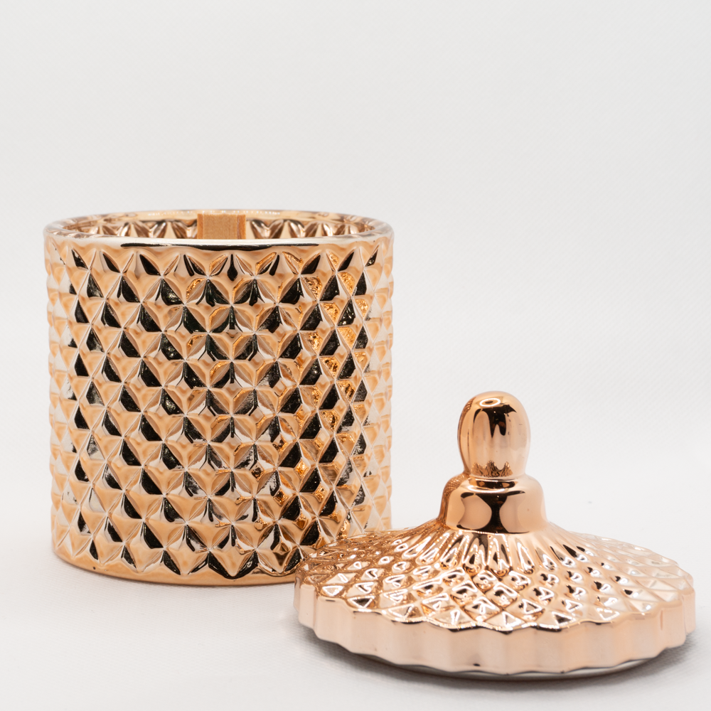 Rose gold candle, with lid placed next to candle and showing a wooden wick within candle. 